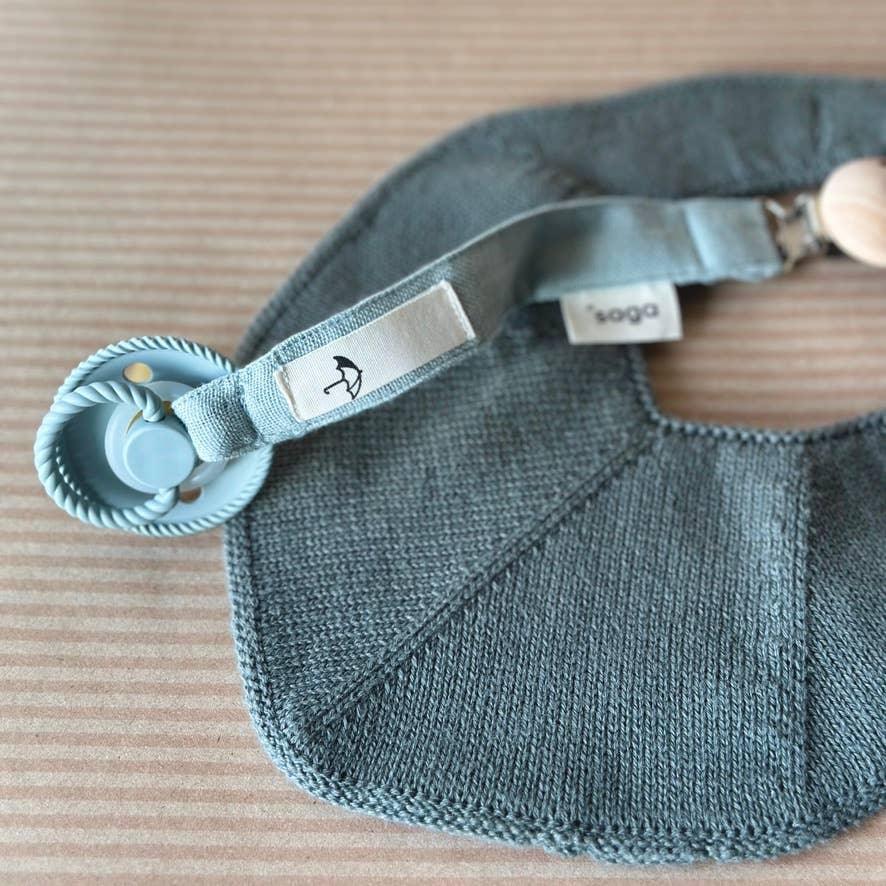 Attache-sucette bio Pala vert poussiereux fixee sur un bavoir pour bebe