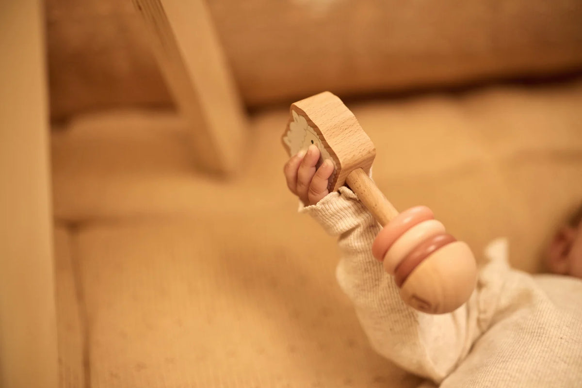 Bebe tenant le hochet en bois naturel alpaga paco Jollein