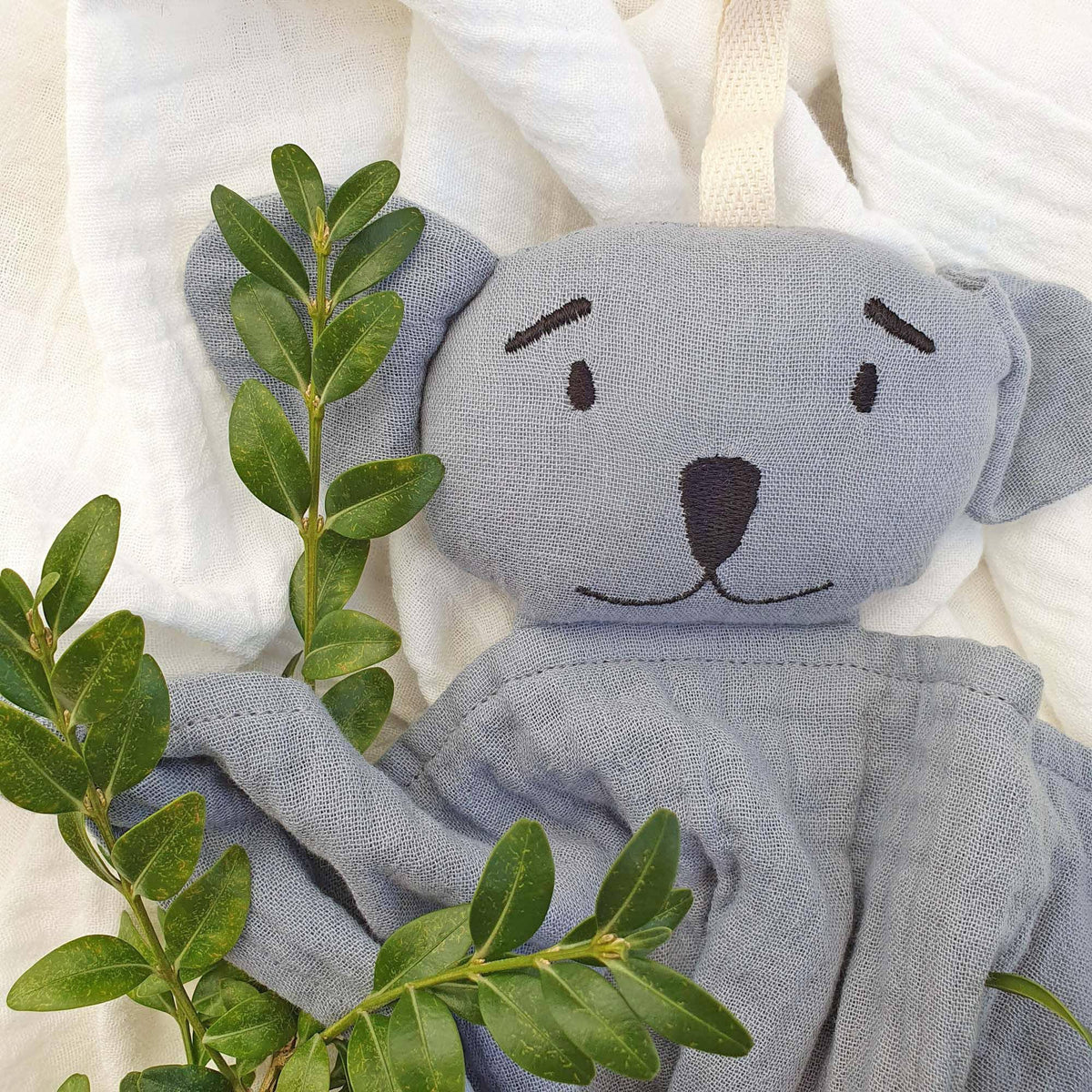 Doudou plat koala en coton biologique Tradewinds pose dans le lit bebe