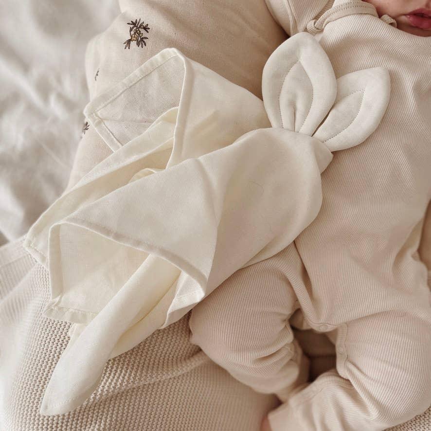 Doudou plat lange creme tenu par un bebe couche